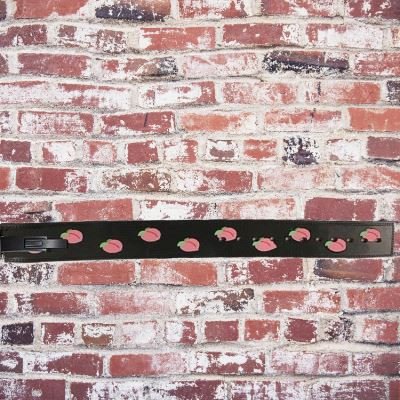 Un élément en cuir noir avec plusieurs perforations alignées et une boucle métallique résistante permettant un réglage sur mesure. L’ensemble est conçu pour assurer un bon maintien et un ajustement sécurisé. L’arrière-plan en briques rouges apporte un con