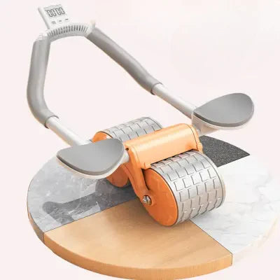 Dispositif d’entraînement compact avec deux roues métalliques et un cadre en plastique renforcé. Repose sur une surface claire. Munie de deux poignées ergonomiques en mousse grise courbée vers le haut. Éclairage uniforme avec un léger reflet sur les roule